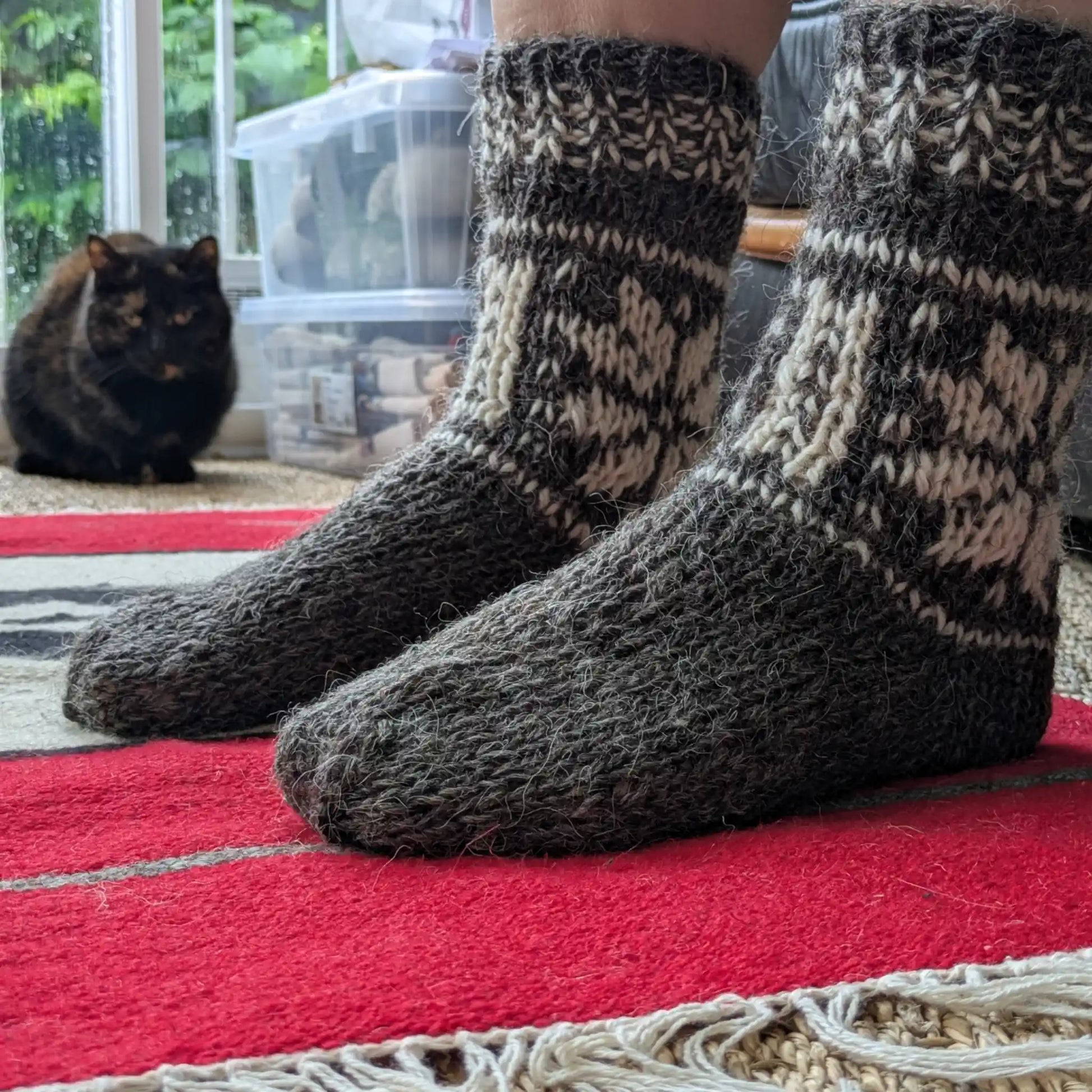 Chaussettes grises en laine de mouton portées en intérieur. Le pied uni contraste avec la tige à motifs écrus. Maille épaisse adaptée aux temps froids.