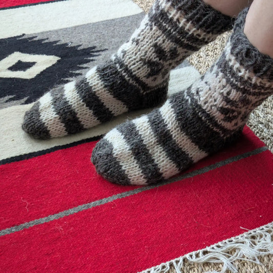 Vue portée de chaussettes grises rayées en laine. La maille est dense, avec motifs clairs sur la tige. Chaussettes en laine de Pologne au style rustique.