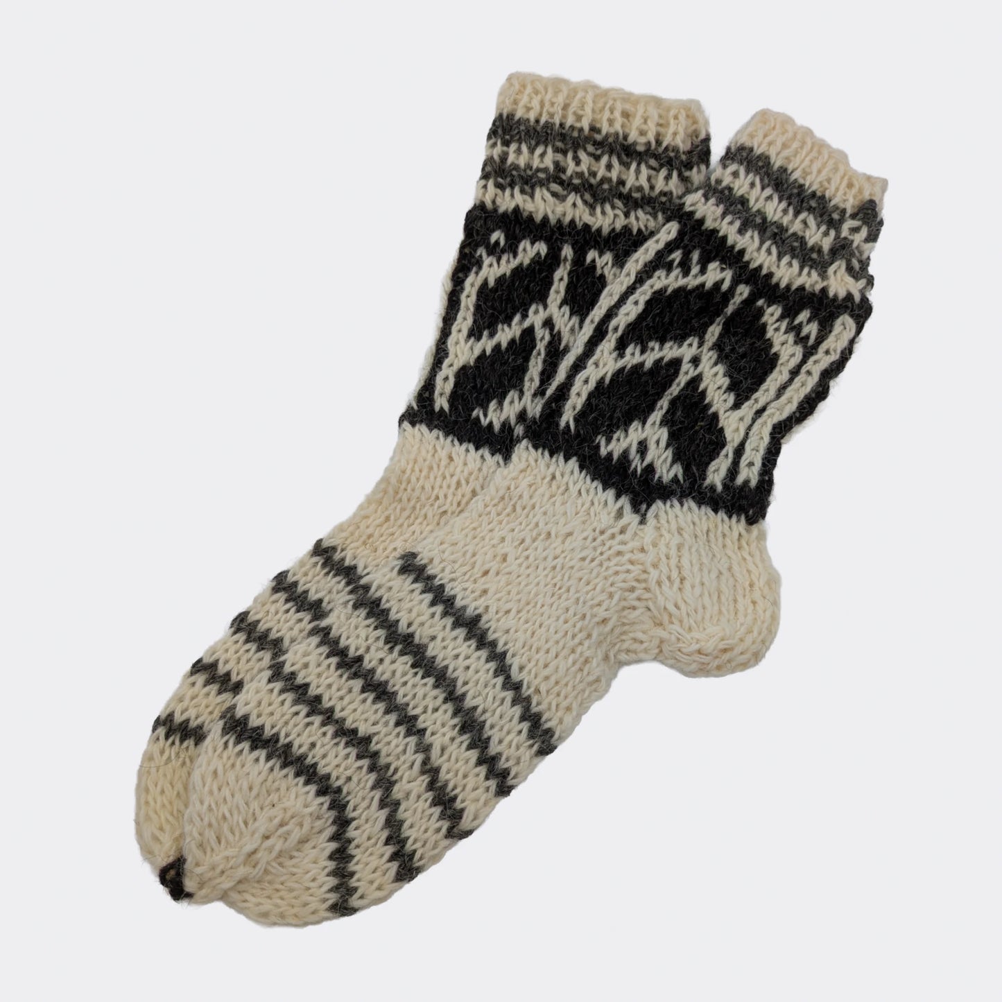Chaussettes artisanales en laine blanche et grise posées à plat. Des rayures diagonales couvrent le pied et des motifs géométriques décorent la tige. Le tricot épais présente un aspect rustique.