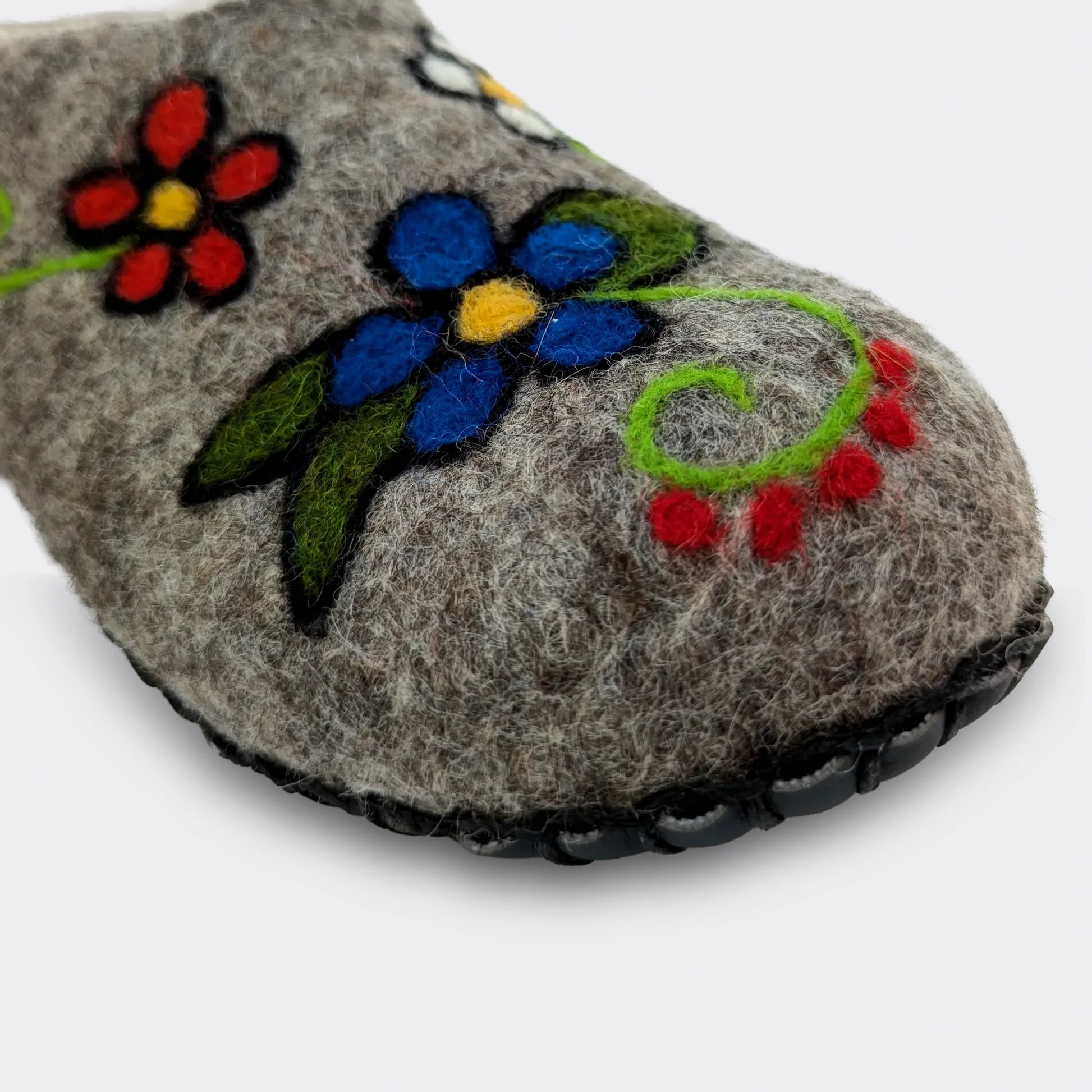 Détail d'un chausson en feutre gris orné de fleurs naïves colorées. Une semelle cousue sur le dessous empêche les glissades. Fabriqué en Serbie en Voïvodine.