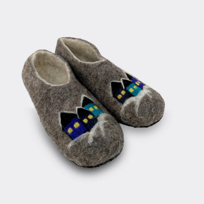 Vue en biais d’un chausson en laine feutrée grise fabriqué en Serbie, décor de village naïf coloré et semelle simili-cuir cousue