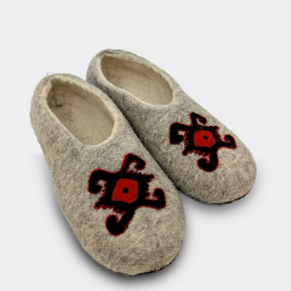 Pantoufle artisanale en laine grise feutrée vue de biais, décorée du motif stylisé d'une tortue. Ce dessin ancien symbolise longévité et stabilité familiale. Vue de biais.
