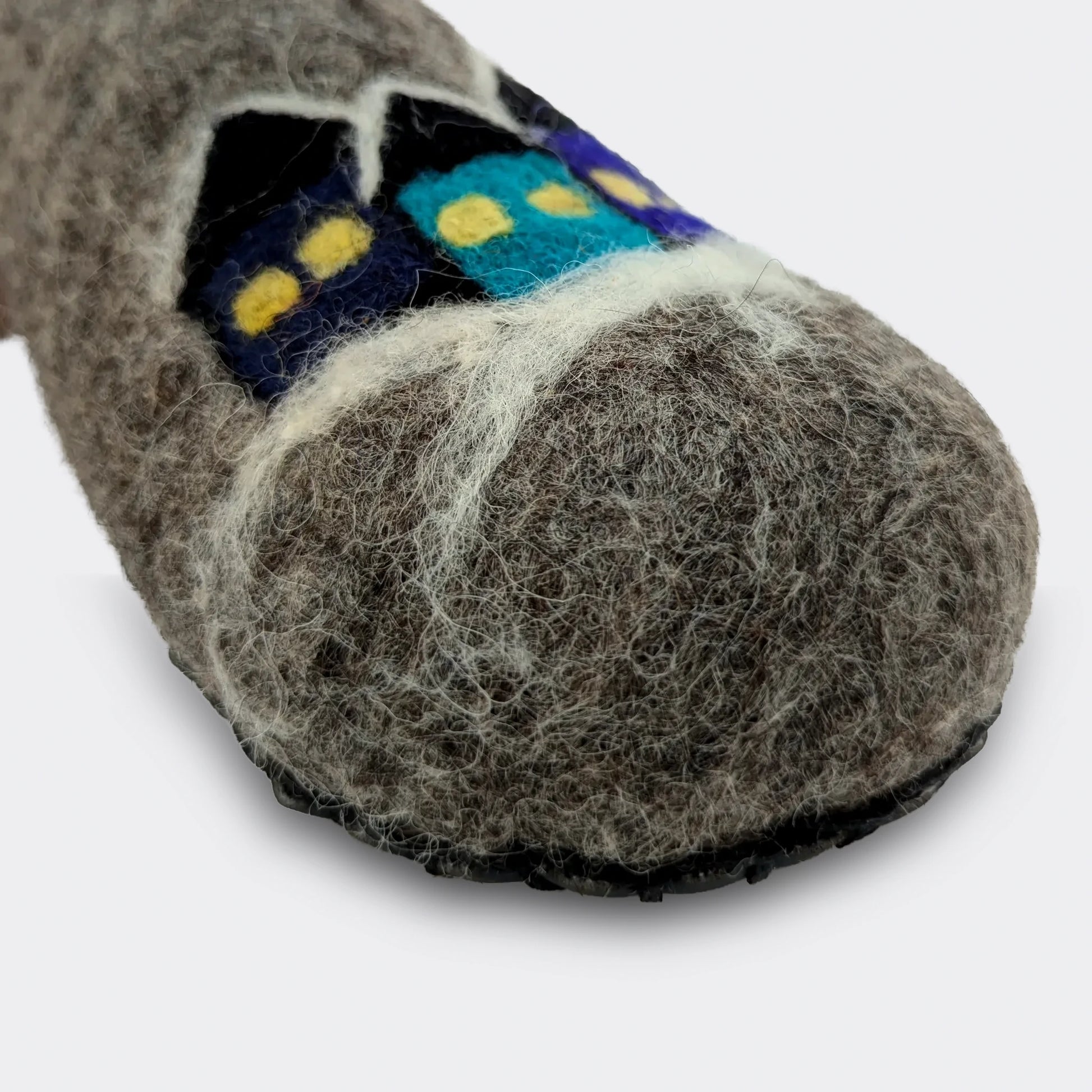 Gros plan d’un motif naïf représentant des maisons sur un chausson artisanal en feutre gris serbe, laine traditionnelle et esthétique folklorique