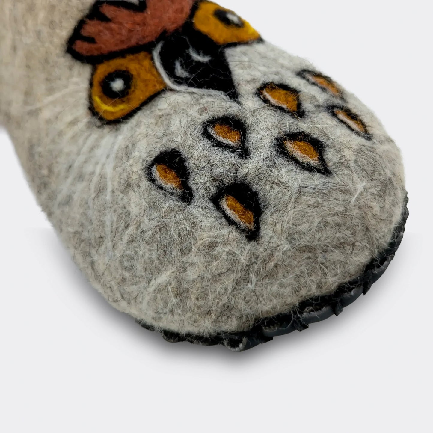 Gros plan sur motif de chouette stylisée décorant un chausson en feutre gris, détail artisanal et couleurs ocres, vue en gros plan.
