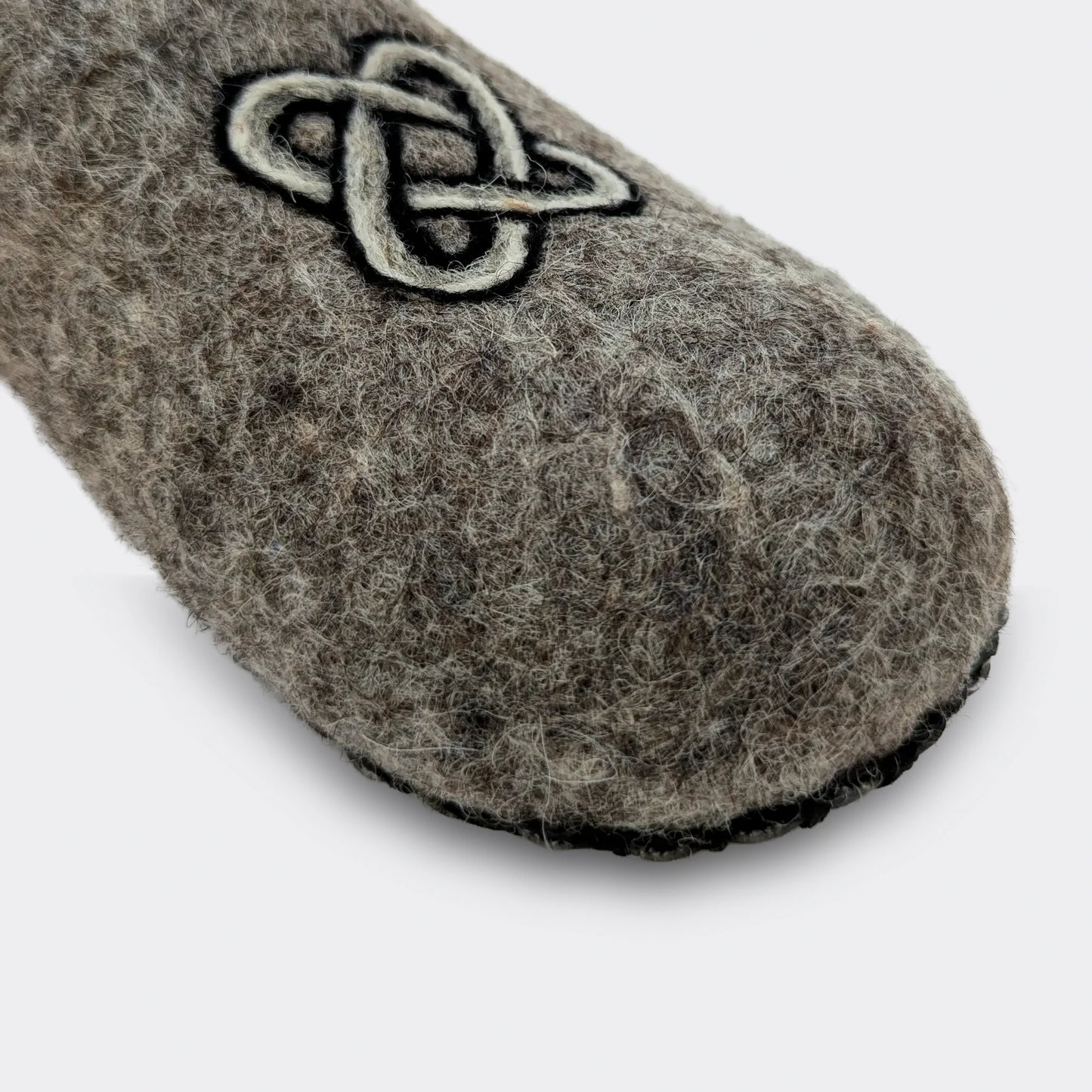 Gros plan sur un chausson en laine grise feutrée agrémenté d'un motif noir et blanc représentant le nœud de Salomon, symbole ancien.