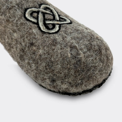 Gros plan sur un chausson en laine grise feutrée agrémenté d'un motif noir et blanc représentant le nœud de Salomon, symbole ancien.