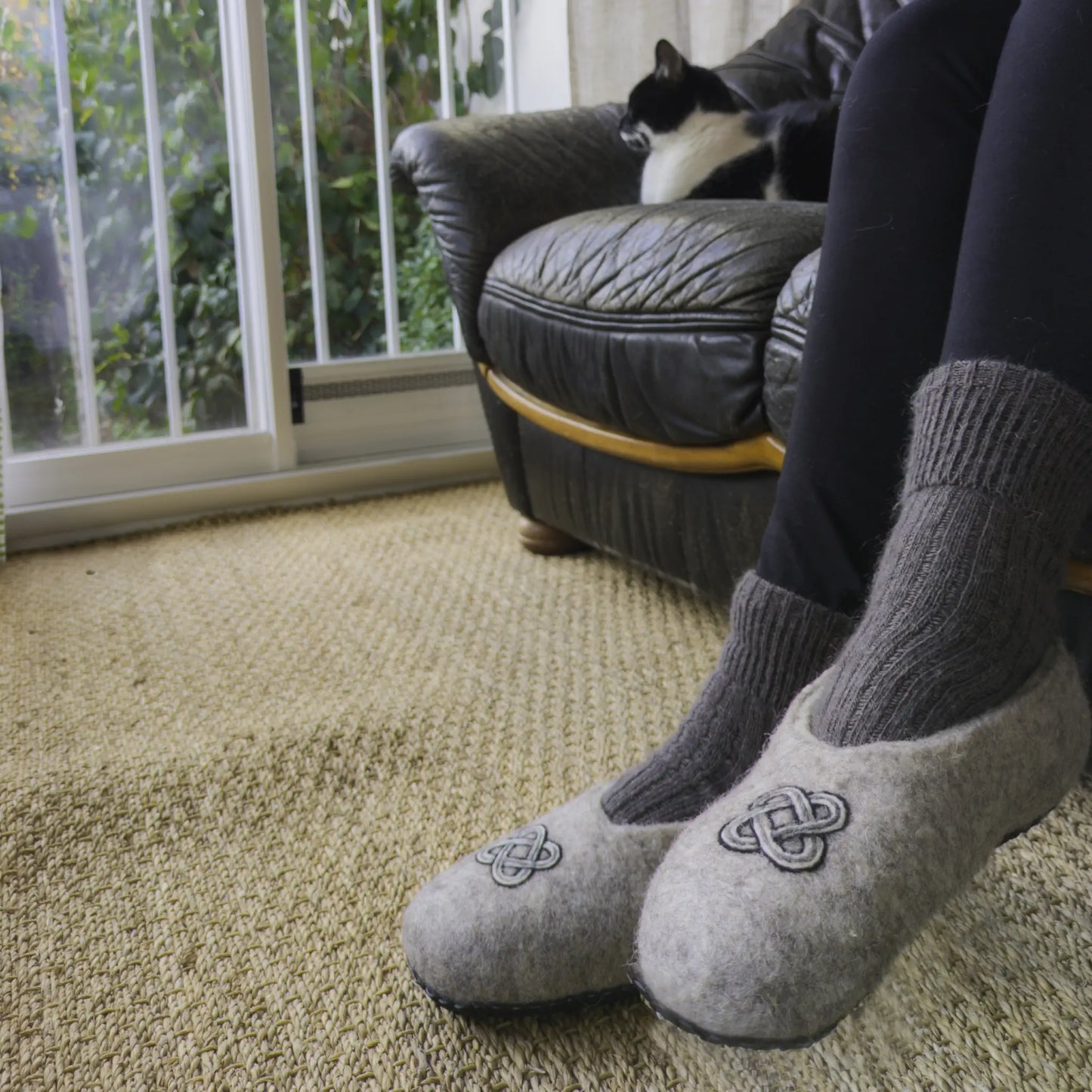 Un nœud de Salomon orne des chaussons en feutre gris, entièrement faits main. Ils sont portés par une personne.