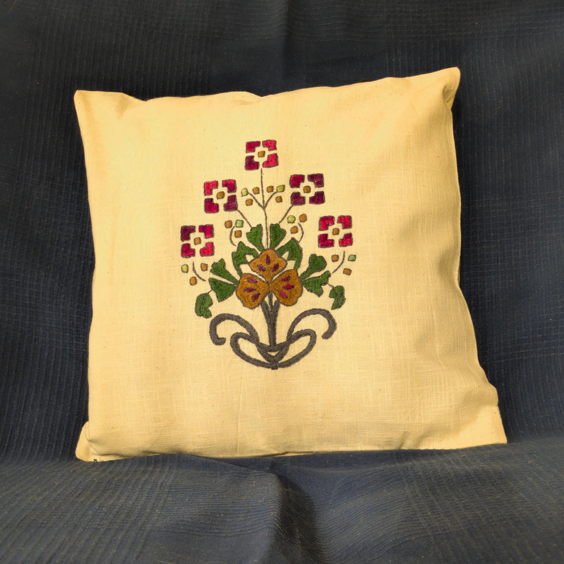 Housse en lin naturel brodée main avec un bouquet composé. Les fleurs géométriques rouges entourent une fleur centrale ocre. Un motif équilibré.