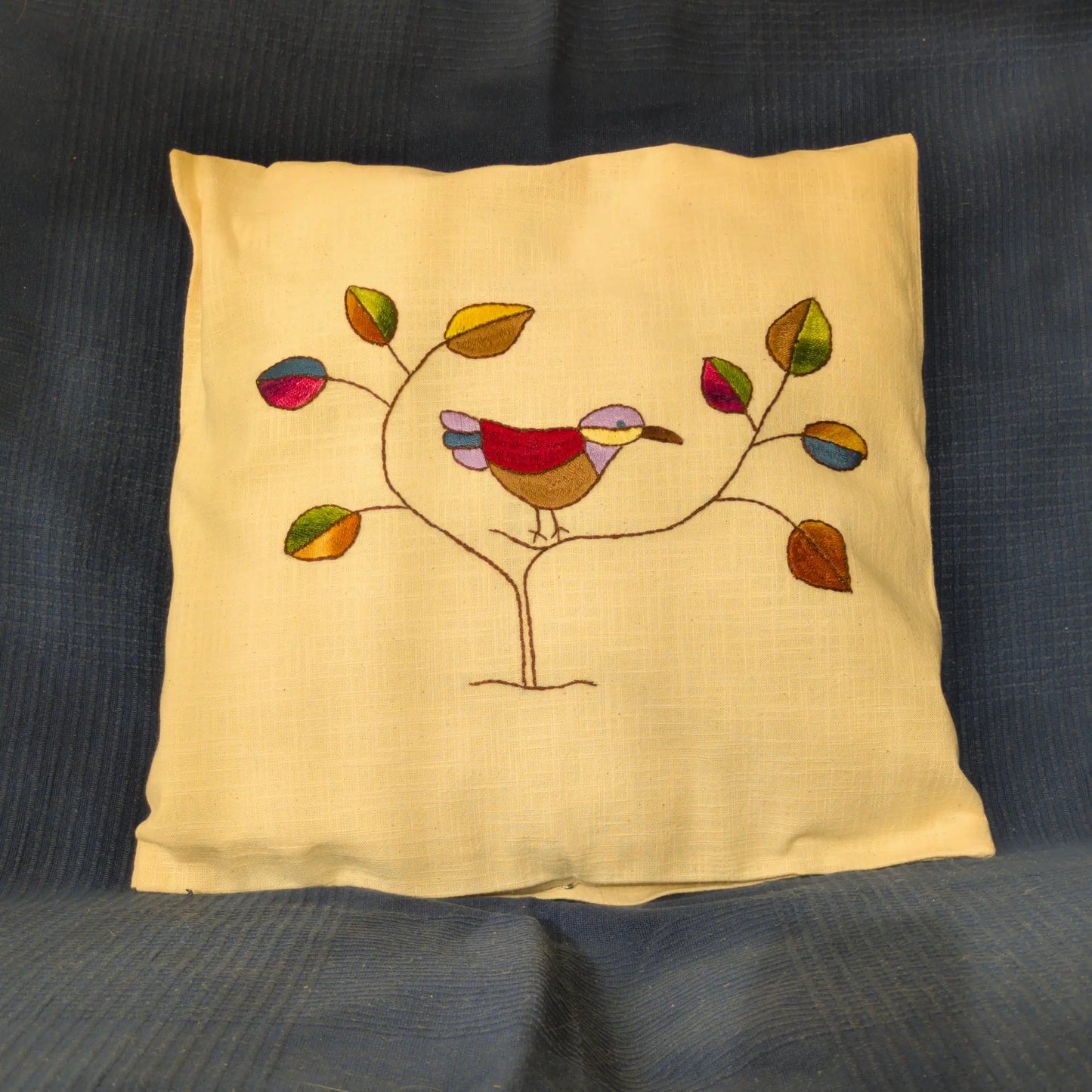 Housse de coussin en lin brodée d’un oiseau stylisé et de feuilles colorées.
