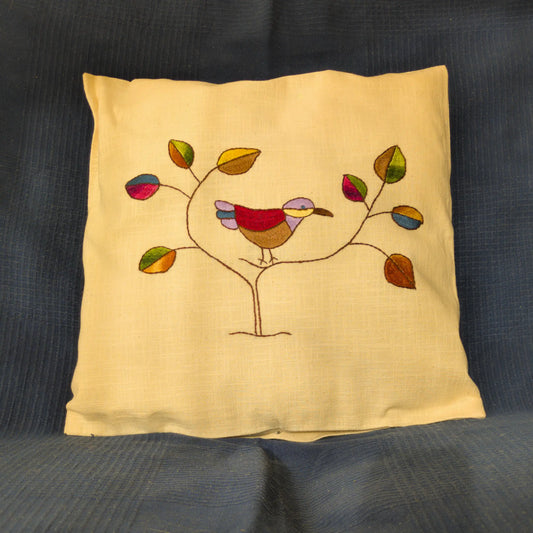 Housse de coussin en lin brodée d’un oiseau stylisé et de feuilles colorées.