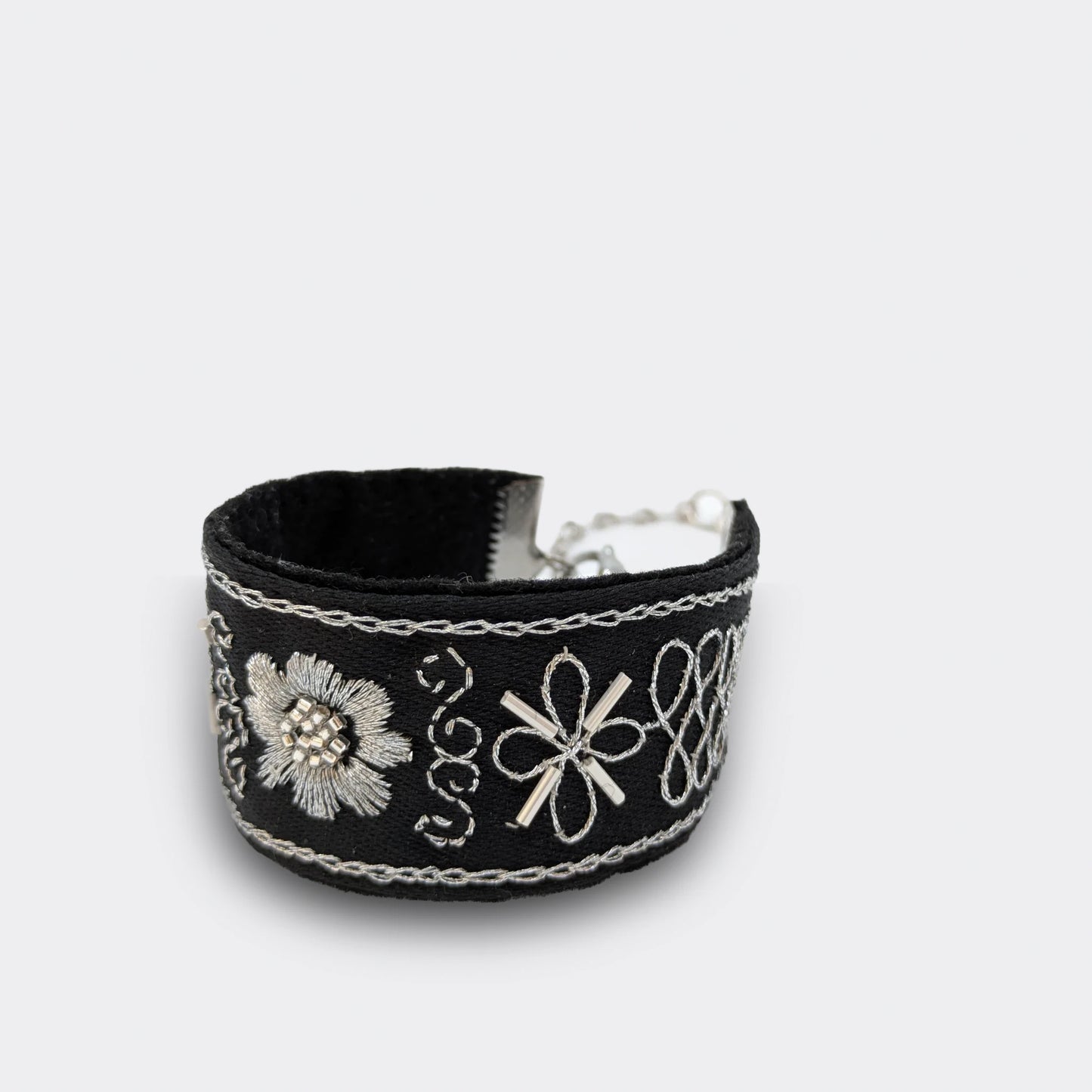 Détail du motif central d’un bracelet brodé noir et argent, fleur stylisée réalisée en point plein et chaînette. Artisanat balkanique inspiré du zlatovez, gros plan.