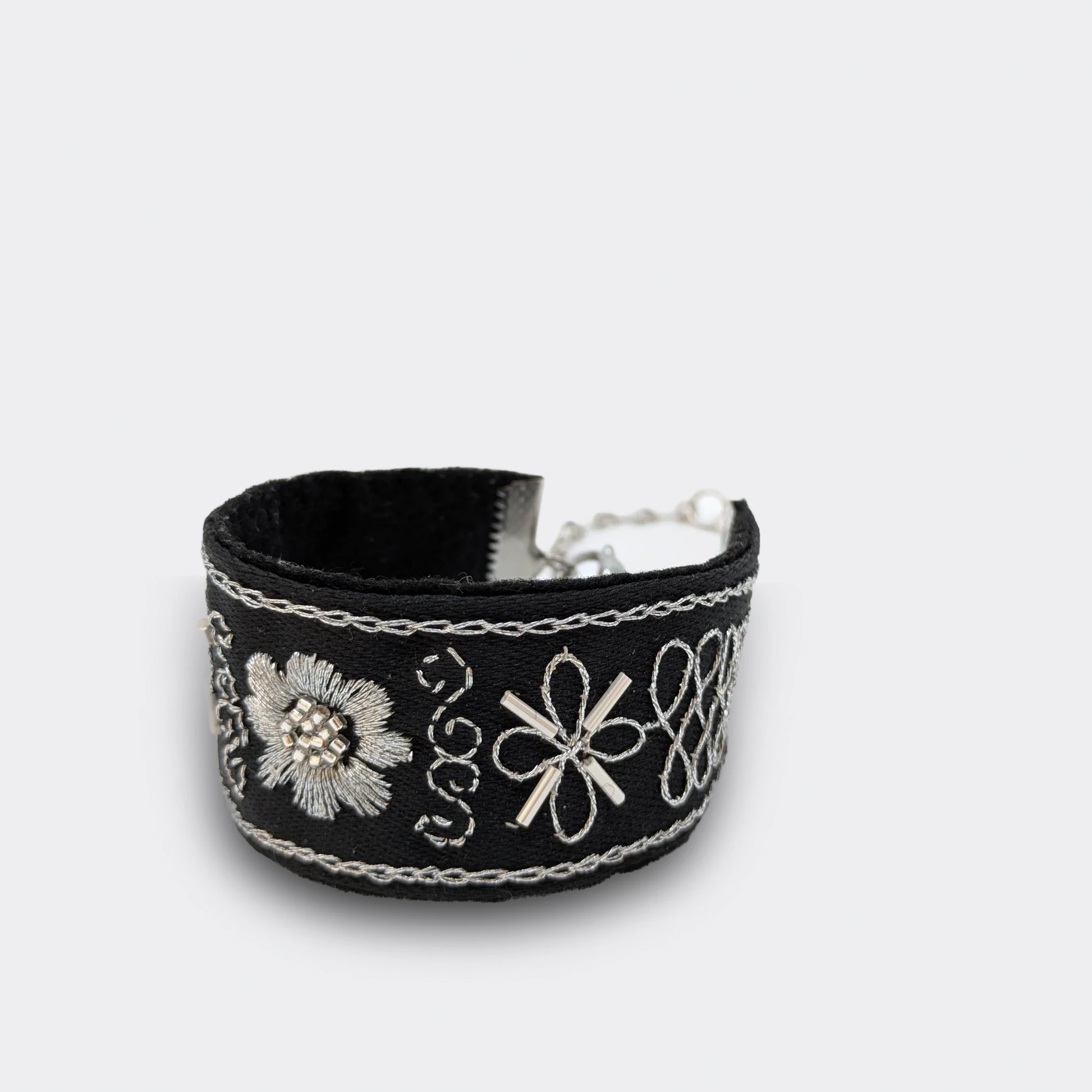 Détail du motif central d’un bracelet brodé noir et argent, fleur stylisée réalisée en point plein et chaînette. Artisanat balkanique inspiré du zlatovez, gros plan.