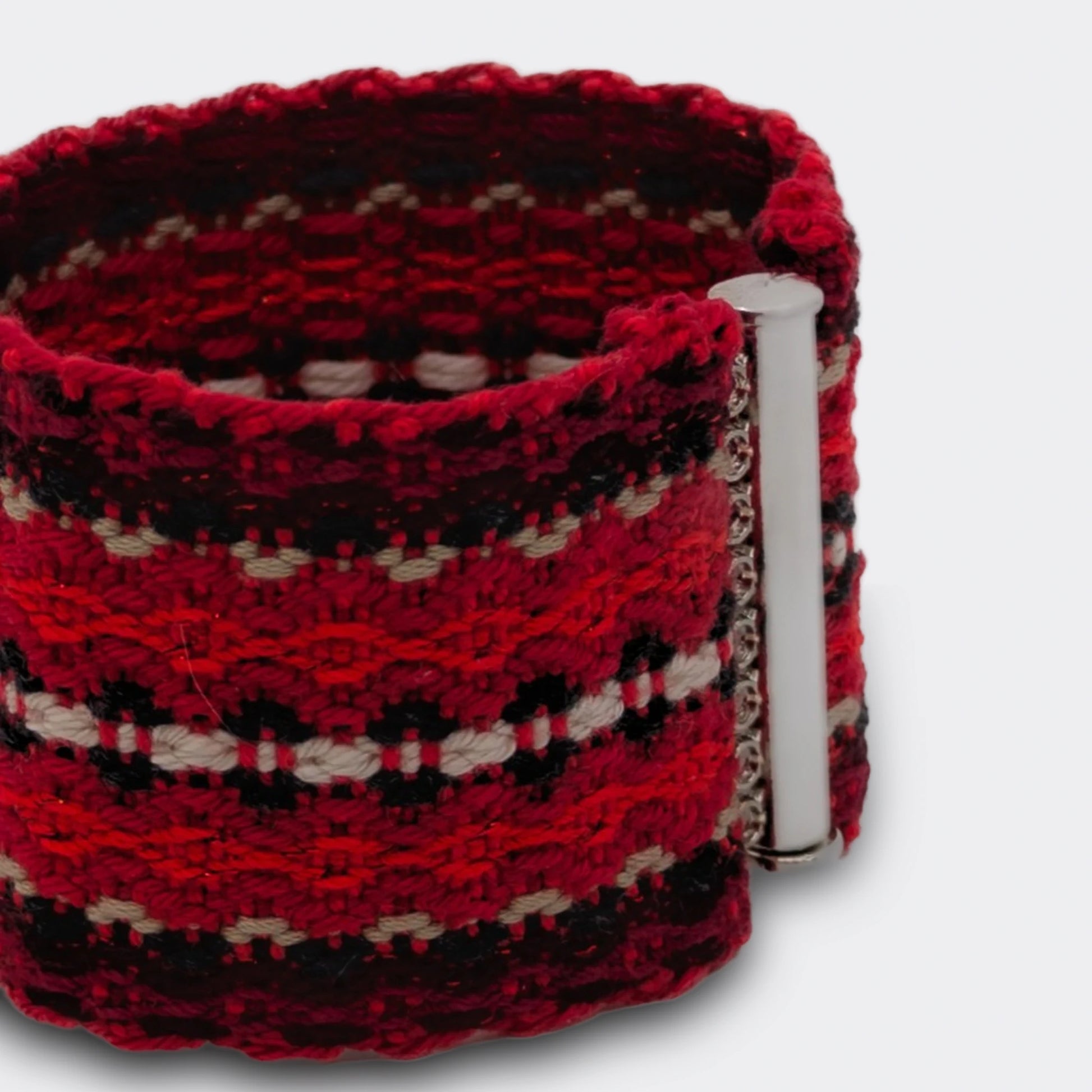 Détail d'un bracelet tissé rouge, ton sur ton, avec une ligne centrale blanche. D'inspiration folklorique des Balkans.