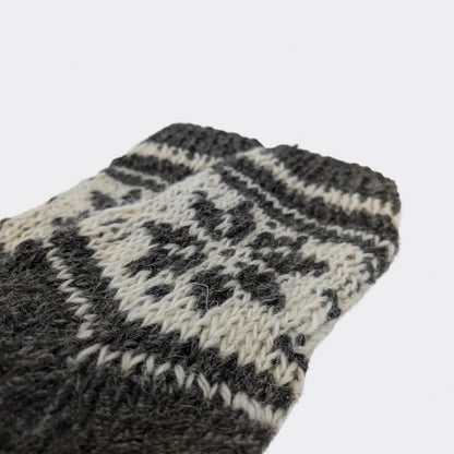 Gros plan sur le haut d’une chaussette grise en laine de mouton. Le motif clair est tricoté dans la maille. Chaussette chaude en laine au style montagnard.