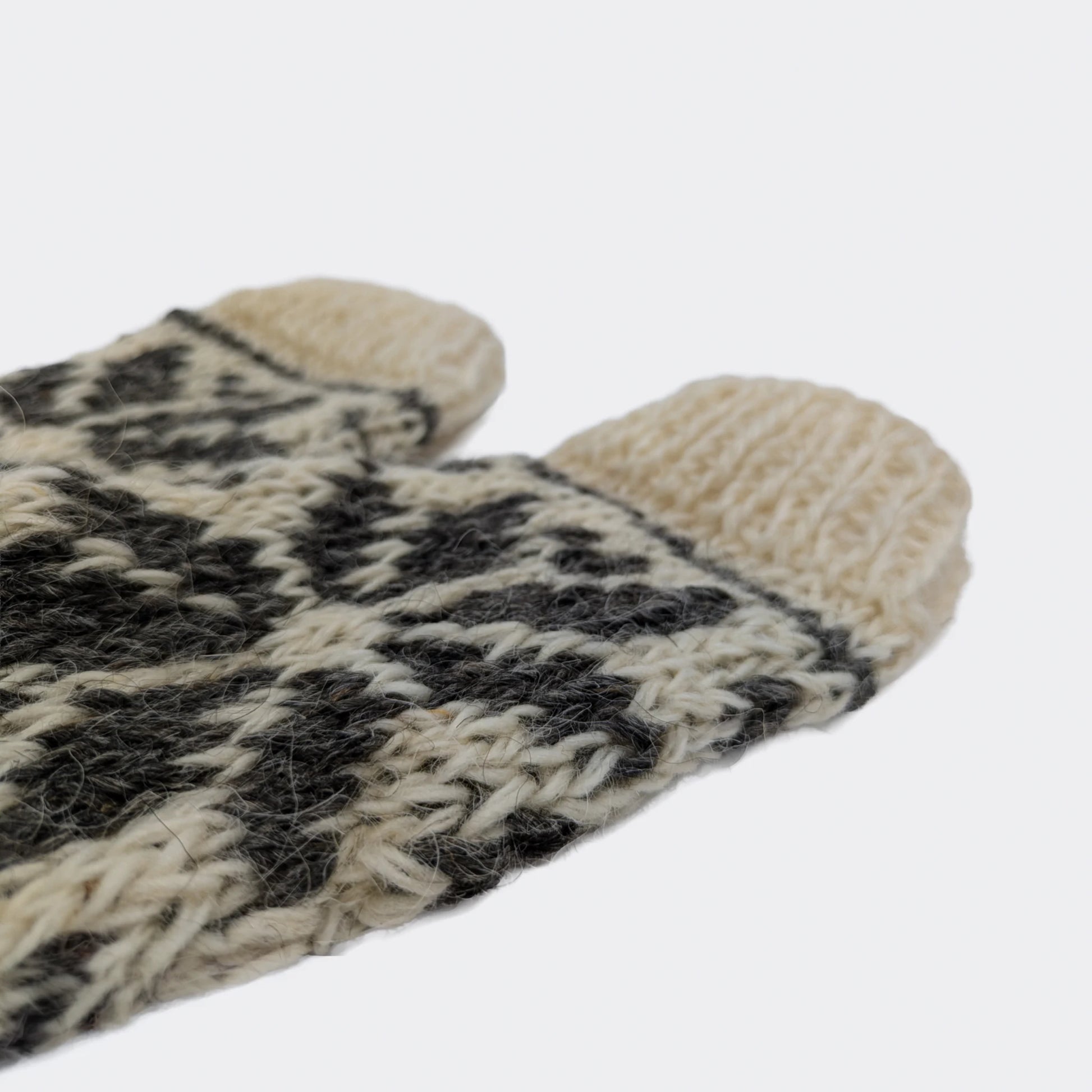 Détail de chaussettes en laine tricotées à la main. La maille blanche et grise forme des motifs géométriques contrastés. Le gros plan montre l’épaisseur et la texture rustique du tricot.