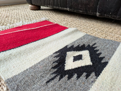 Zoom sur le tapis monténégrin rouge et gris. Fibres de laine visibles et motif géométrique traditionnel. Couleurs contrastées.