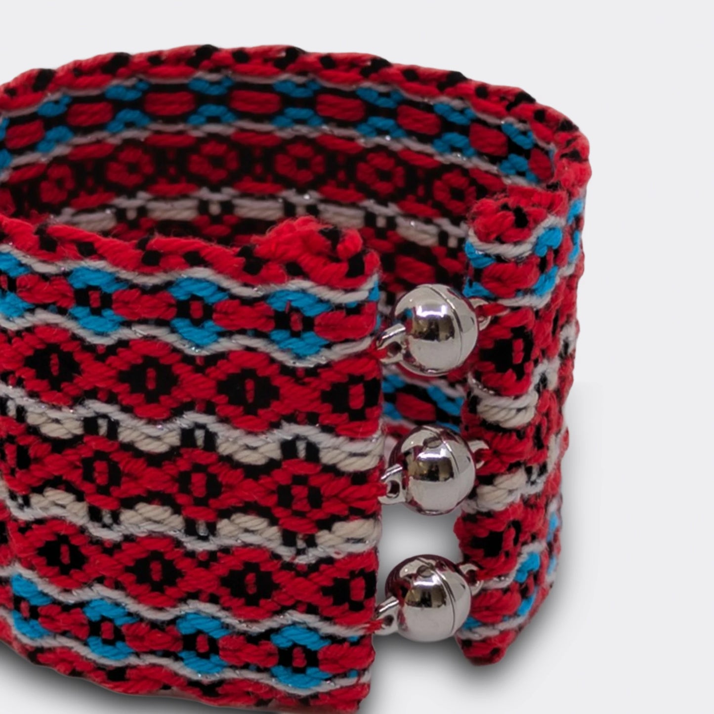 Gros plan sur la texture tissée du bracelet, entrecroisement des fils rouges et bleus, héritage textile traditionnel des pays de l'est.