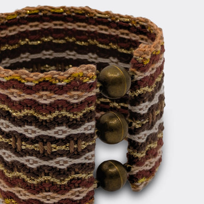 Gros plan sur la structure tissée du bracelet, reflets or et nuances brunes