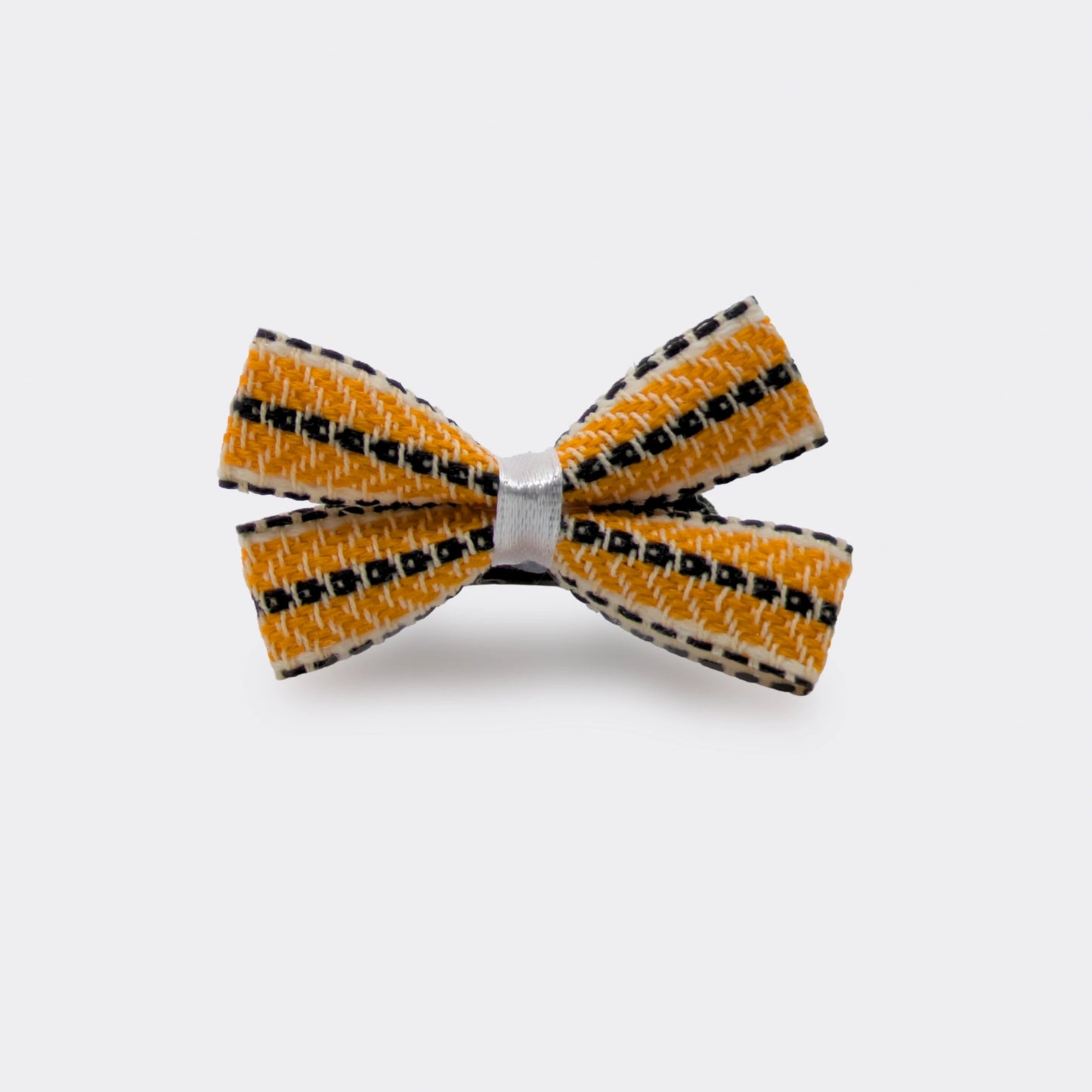 Nœud papillon orange fixé sur un élastique cheveux noir. Le tissu tissé crée un motif régulier. Un accessoire discret pour coiffure simple.