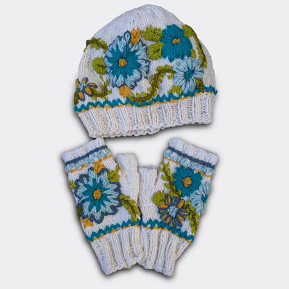 Ensemble artisanal bonnet et mitaines tricotés main, fond blanc cassé, décor floral bleu et turquoise crocheté.