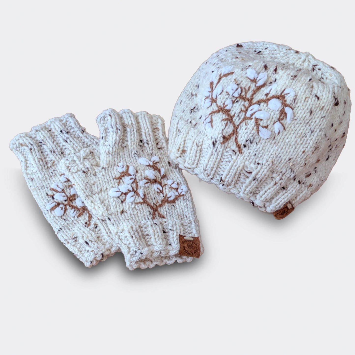 Ensemble bonnet et mitaines écru moucheté tricoté main, avec branches de coton stylisées brodées.