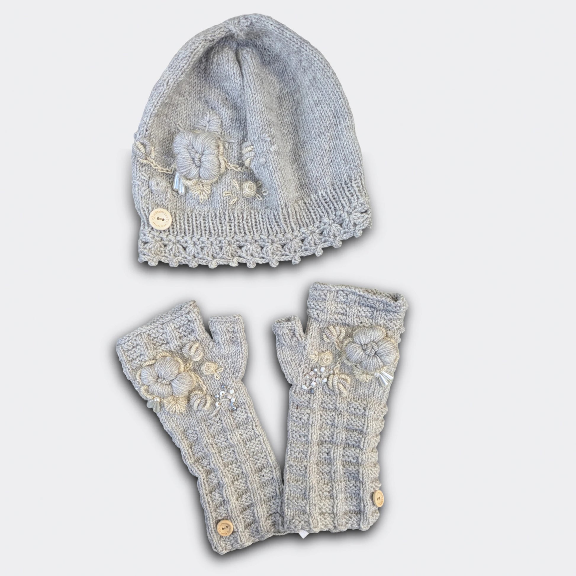 Ensemble artisanal tricoté main gris clair, bonnet et mitaines décorés de fleurs beige-écru.