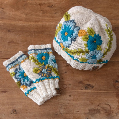 Bonnet et mitaines assortis blanc cassé posés à plat, avec décor floral bleu et turquoise.