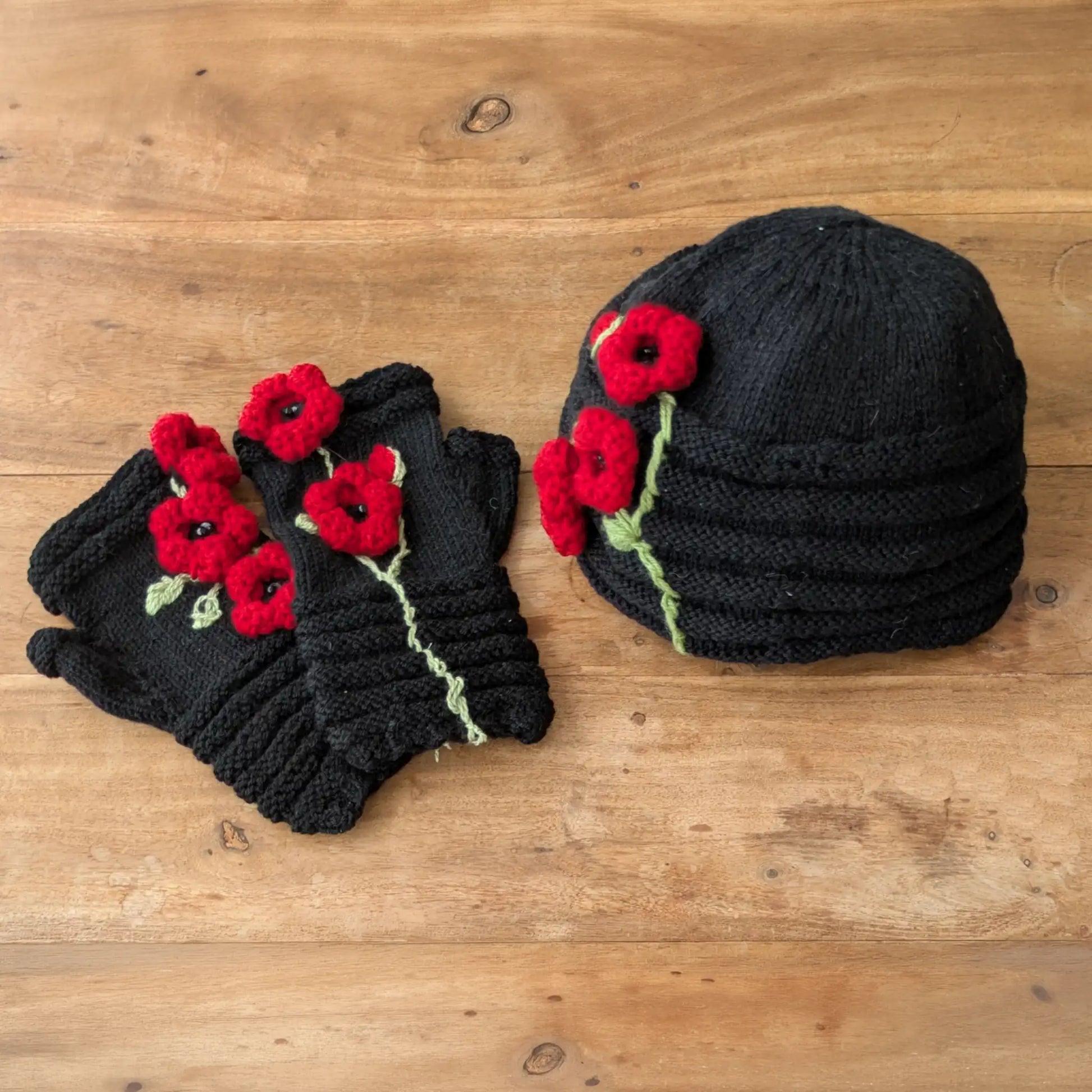 Bonnet et mitaines assortis noirs posés à plat, décorés de grands coquelicots rouges en relief.