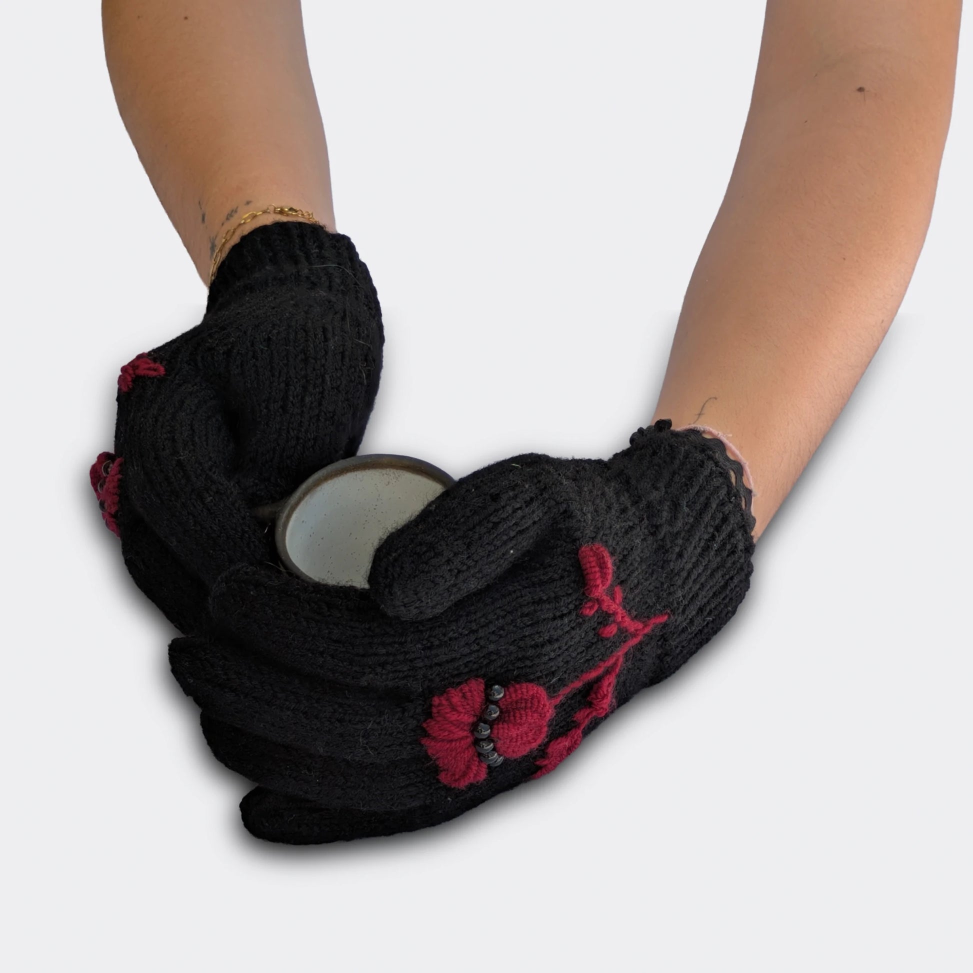 Gants noirs tenant une tasse, décorés d’un chardon pourpre brodé, de petites perles noires et d’un bord côtelé.