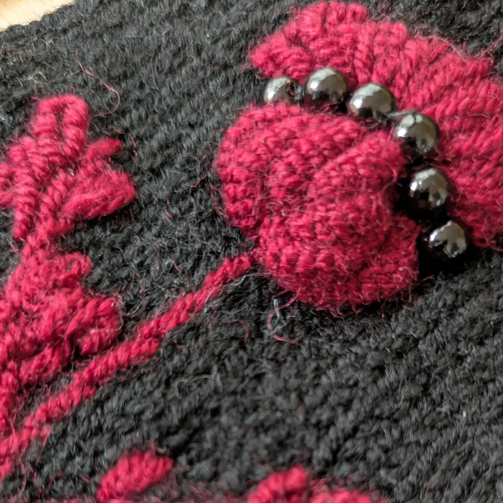 Détail des perles noires cousues sur le chardon pourpre en relief de ces gants noirs.
