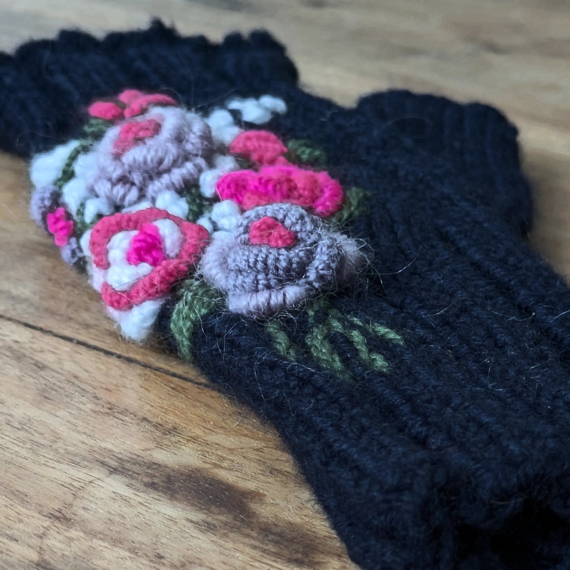 Gros plan sur les fleurs en relief et les tiges vertes brodées de ces gants sans doigts bleu nuit.
