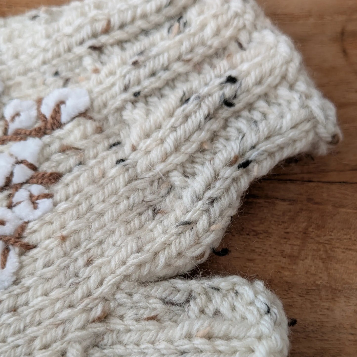 Gros plan sur la maille écru mouchetée et le bord en côtes de ces gants sans doigts faits main.