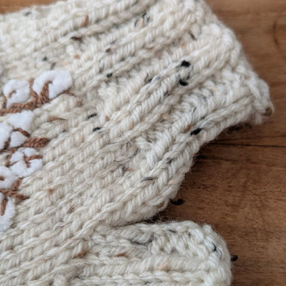 Gros plan sur la maille écru mouchetée et le bord en côtes de ces gants sans doigts faits main.