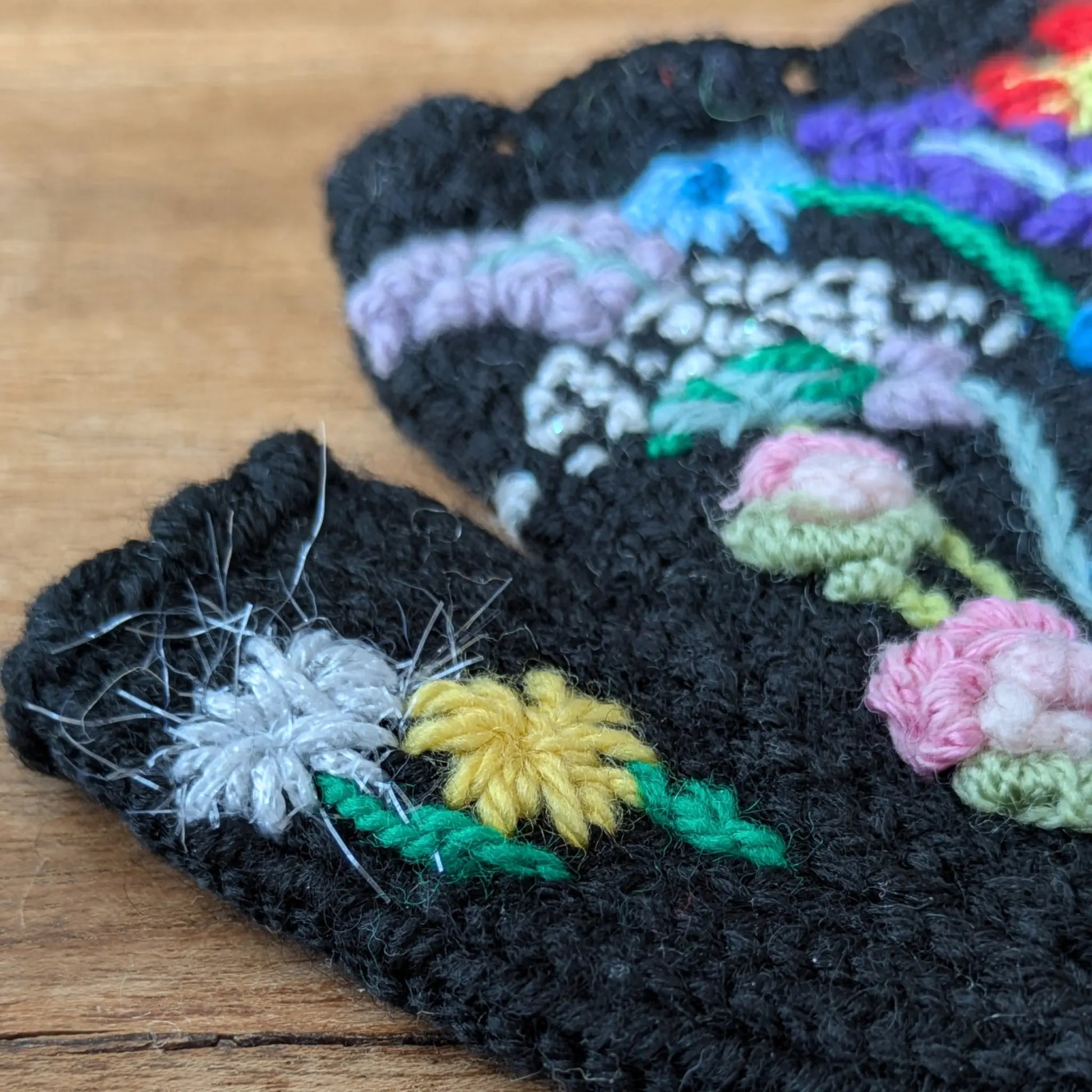 Gros plan sur les fleurs colorées crochetées sur ces gants sans doigts noirs.
