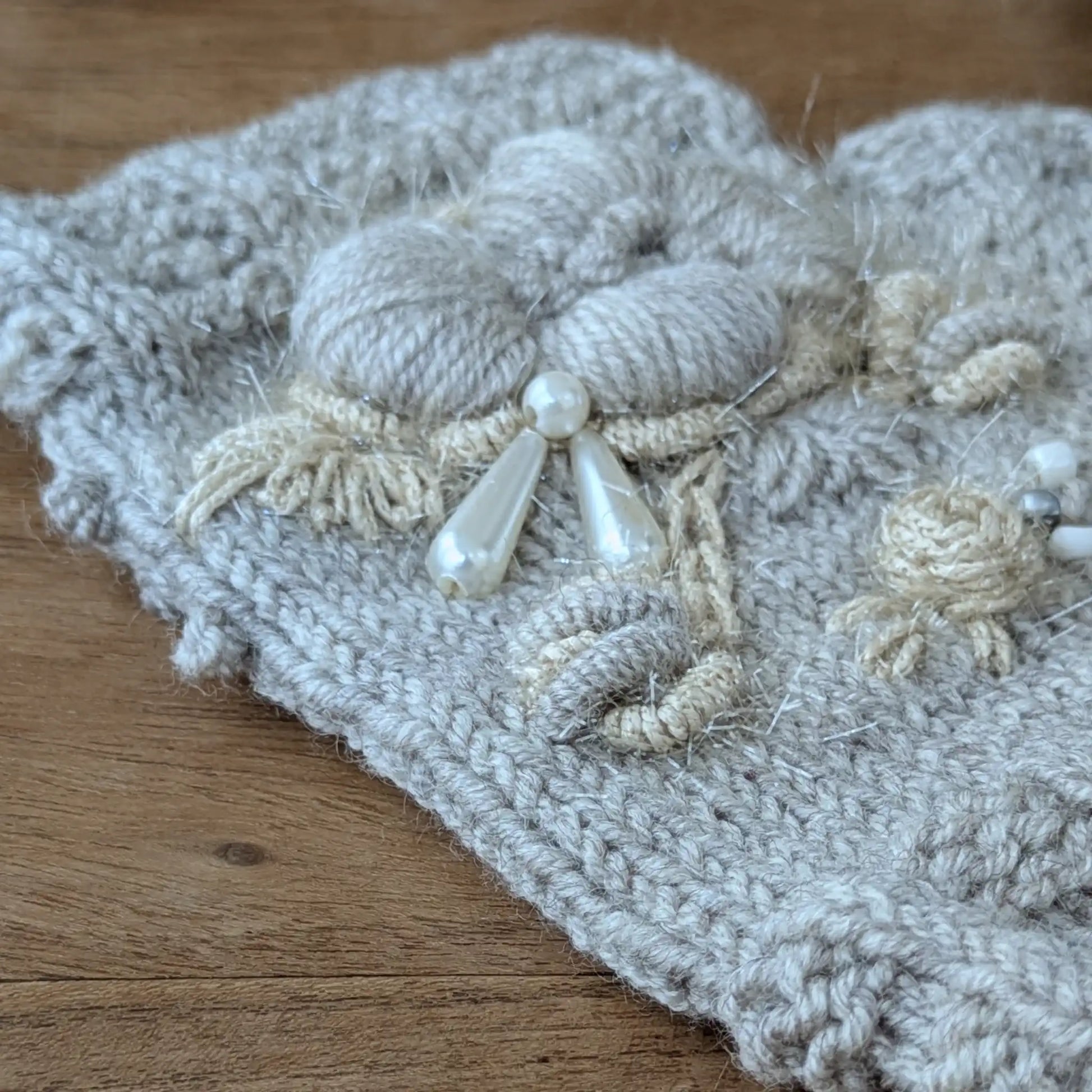 Détail des fleurs écrues et des perles translucides sur des gants sans doigts gris clair assortis au bonnet.