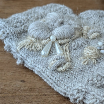 Détail des fleurs écrues et des perles translucides sur des gants sans doigts gris clair assortis au bonnet.