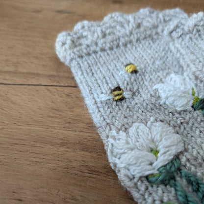 Gros plan sur les crocus blancs crochetés et les abeilles brodées de ces gants sans doigts gris perle.