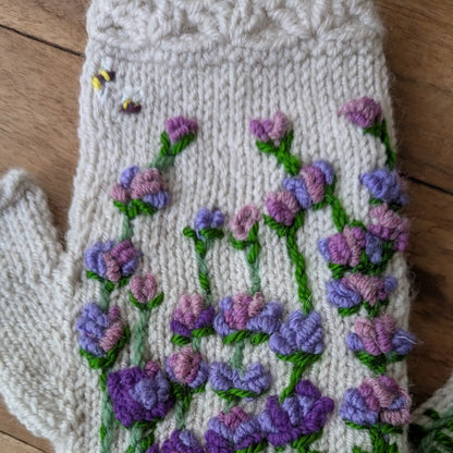 Gros plan sur les fleurs mauves et violettes brodées sur des gants sans doigts gris clair.