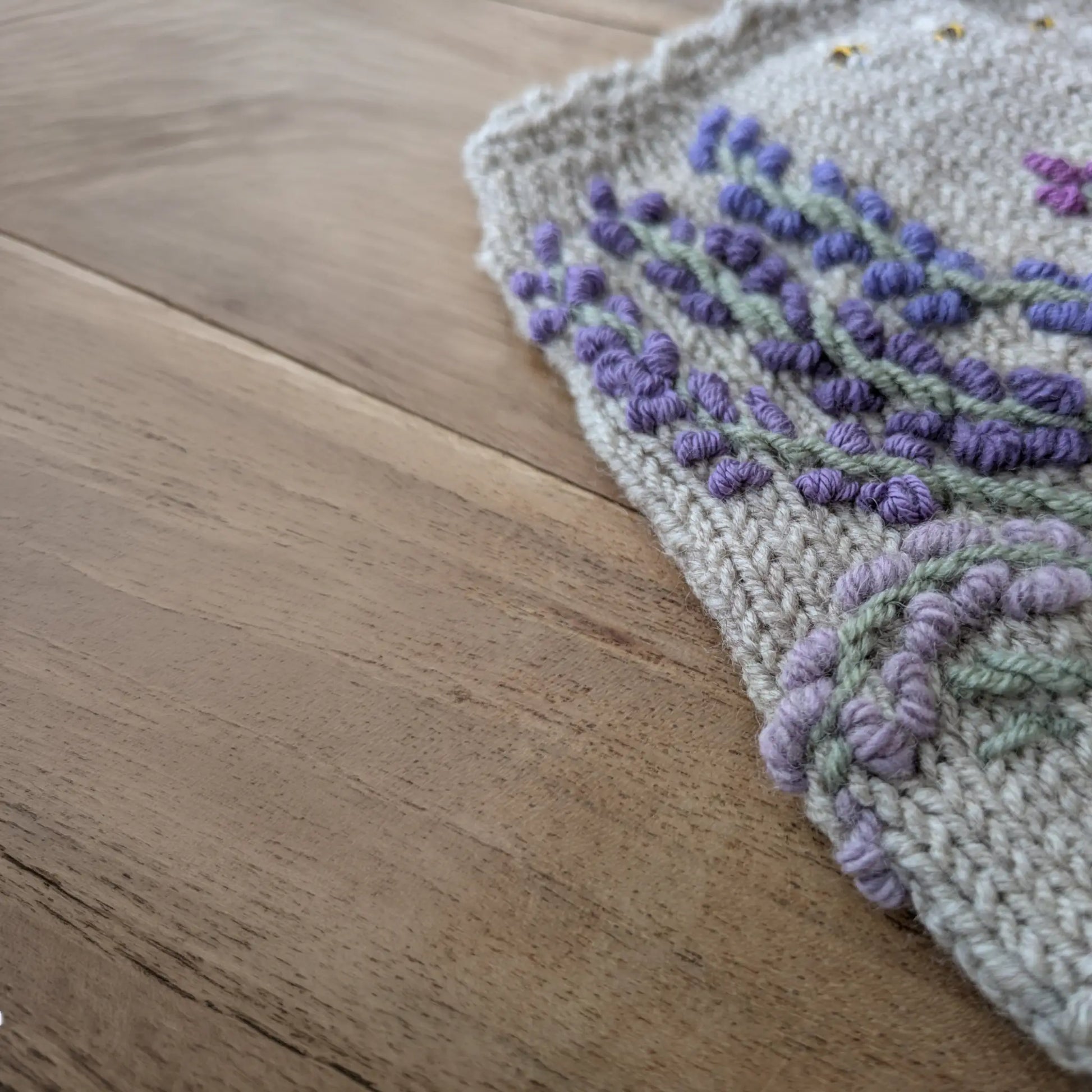 Détail du motif lavande brodé et du bord festonné sur des gants sans doigts gris perle.