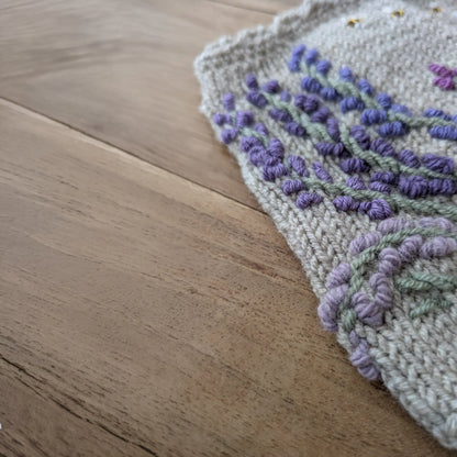 Détail du motif lavande brodé et du bord festonné sur des gants sans doigts gris perle.