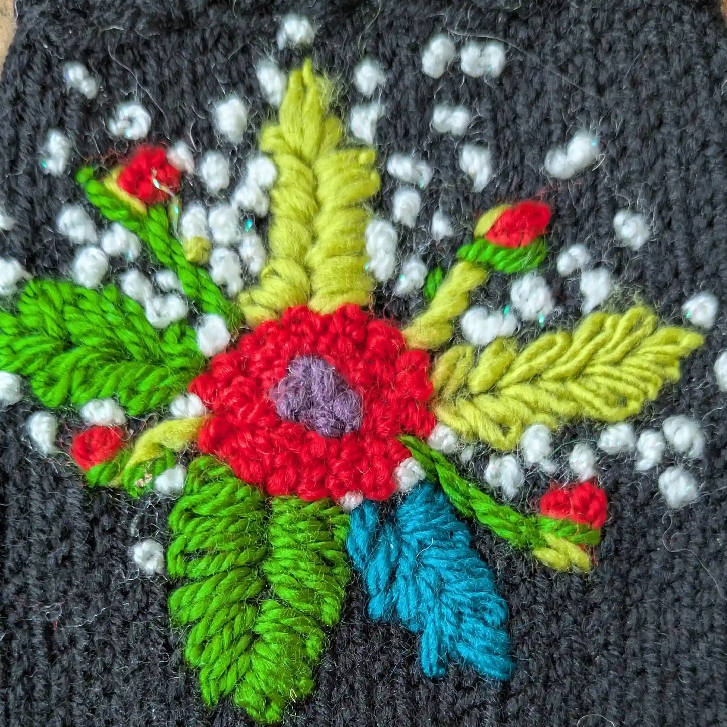 Gros plan sur les fleurs colorées crochetées et les tiges brodées de ces gants sans doigts noirs.