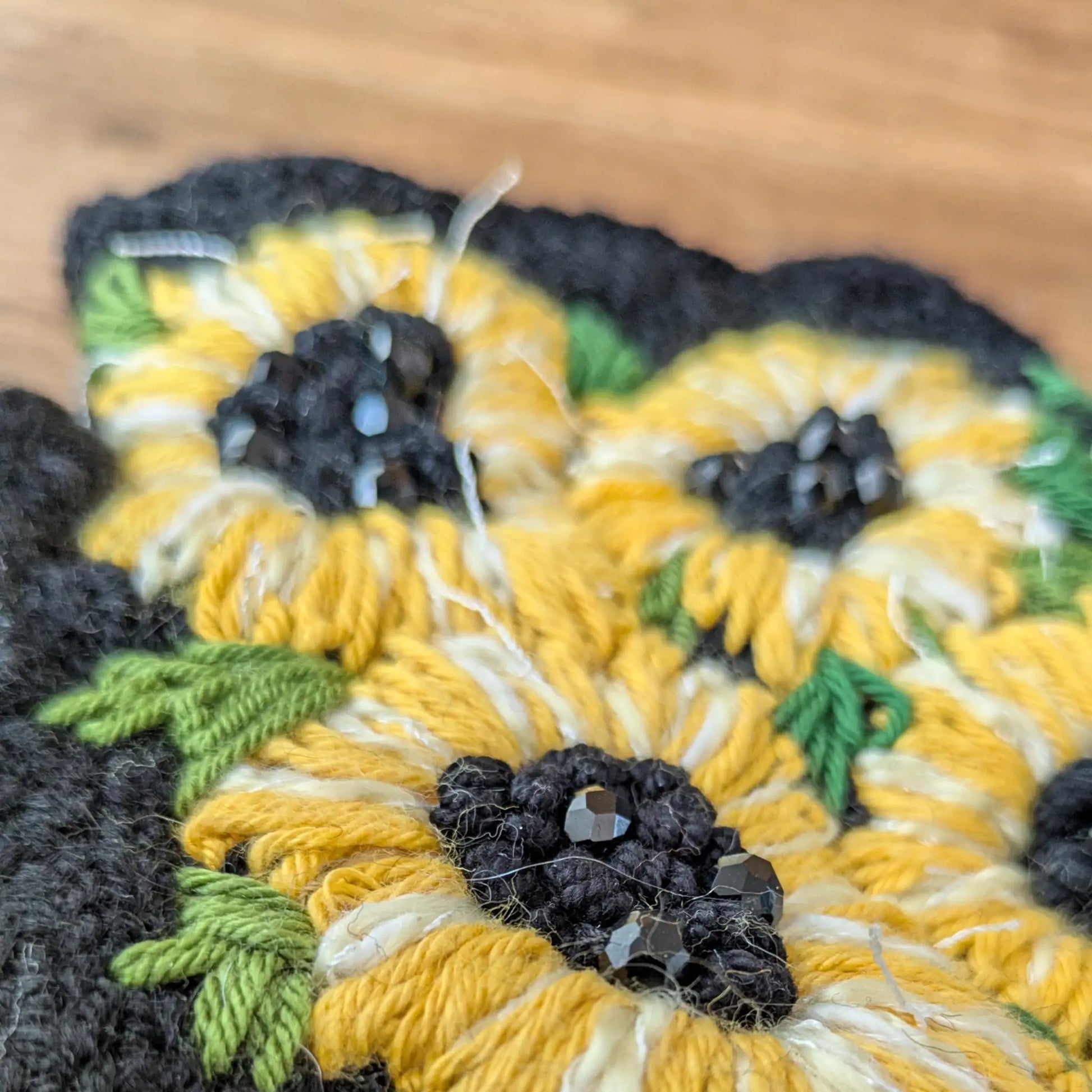 Gros plan sur les tournesols jaunes appliqués et les perles noires au cœur de ces gants sans doigts noirs.