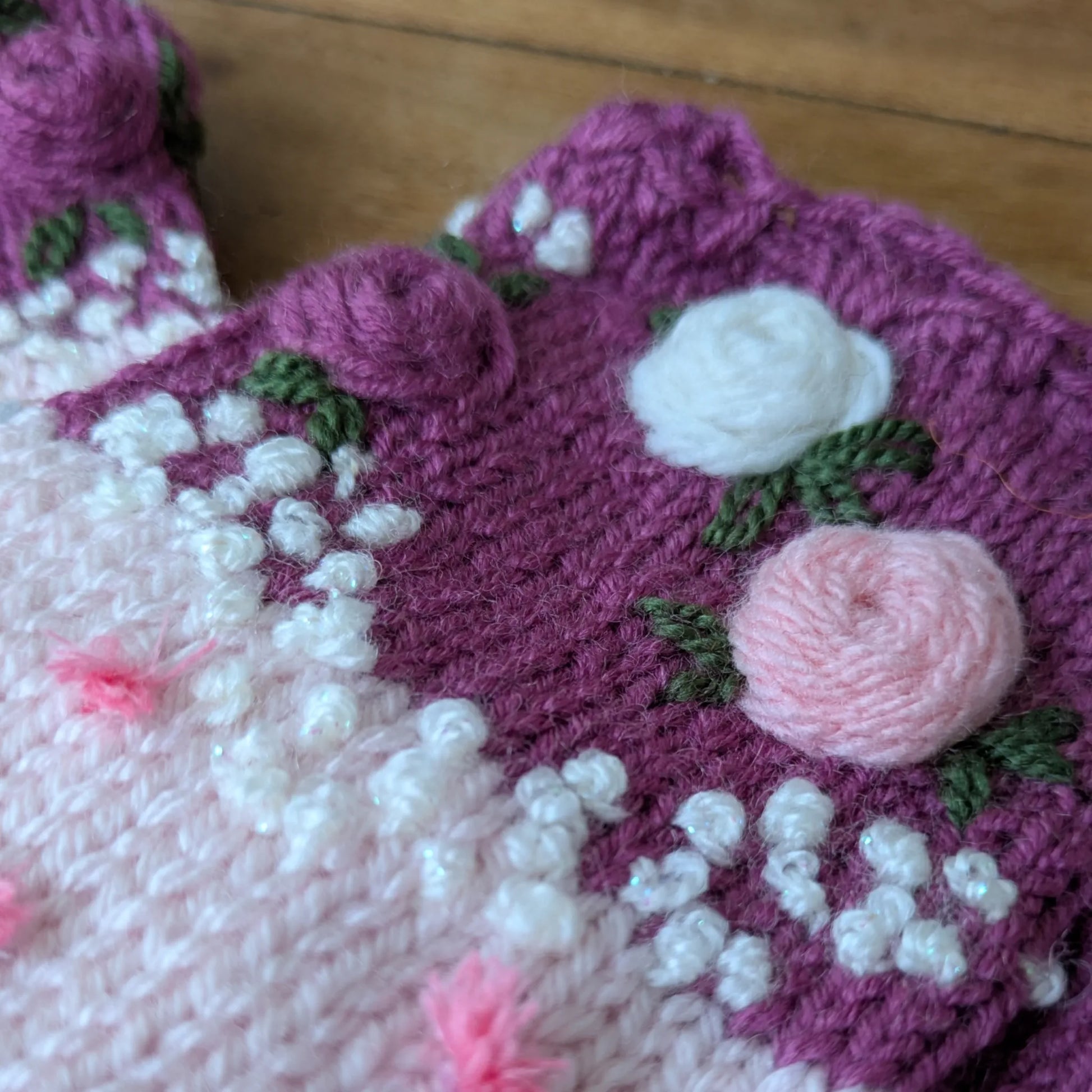 Gros plan sur les roses pastel crochetées et les broderies végétales de ces gants sans doigts roses.