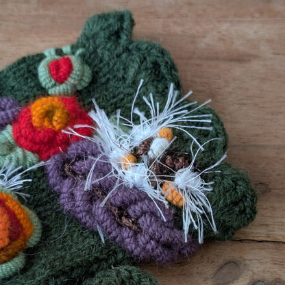 Gros plan sur les fleurs colorées et le bord supérieur festonné de ces gants sans doigts vert olive.