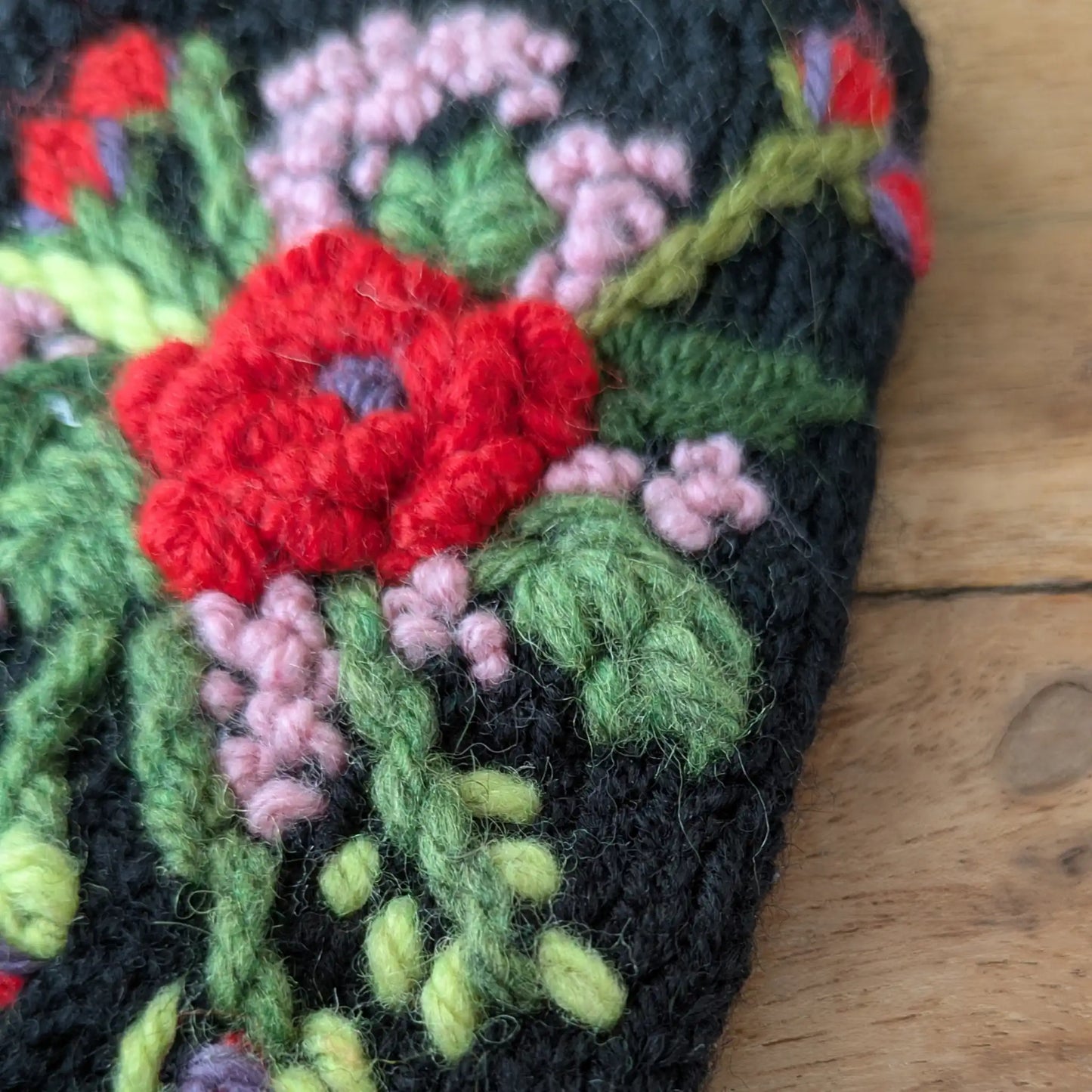 Gros plan sur les fleurs rouges et roses en relief de ces gants sans doigts noirs.