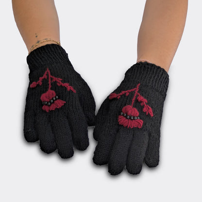 Gants tricotés main sur fond noir, portés à plat, avec motif de chardon pourpre et tiges brodées.