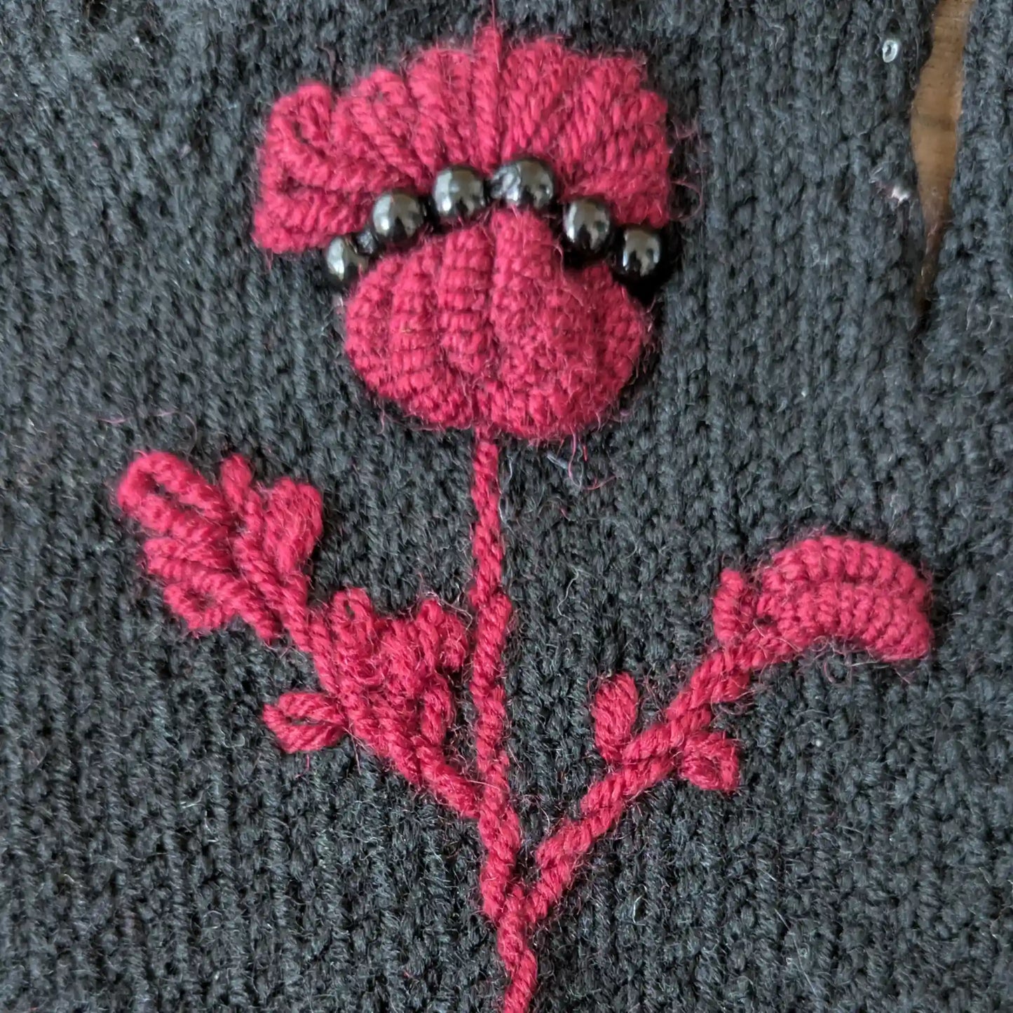 Gros plan sur le chardon pourpre crocheté et brodé main sur des gants noirs tricotés main.