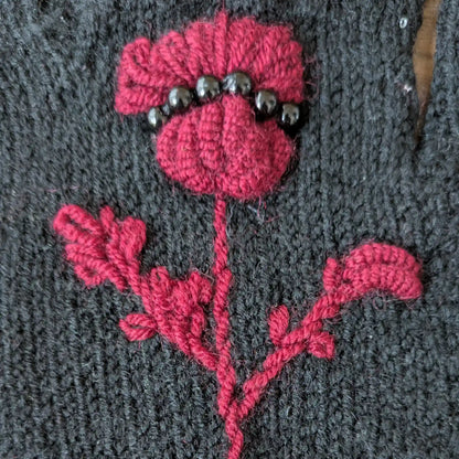 Gros plan sur le chardon pourpre crocheté et brodé main sur des gants noirs tricotés main.
