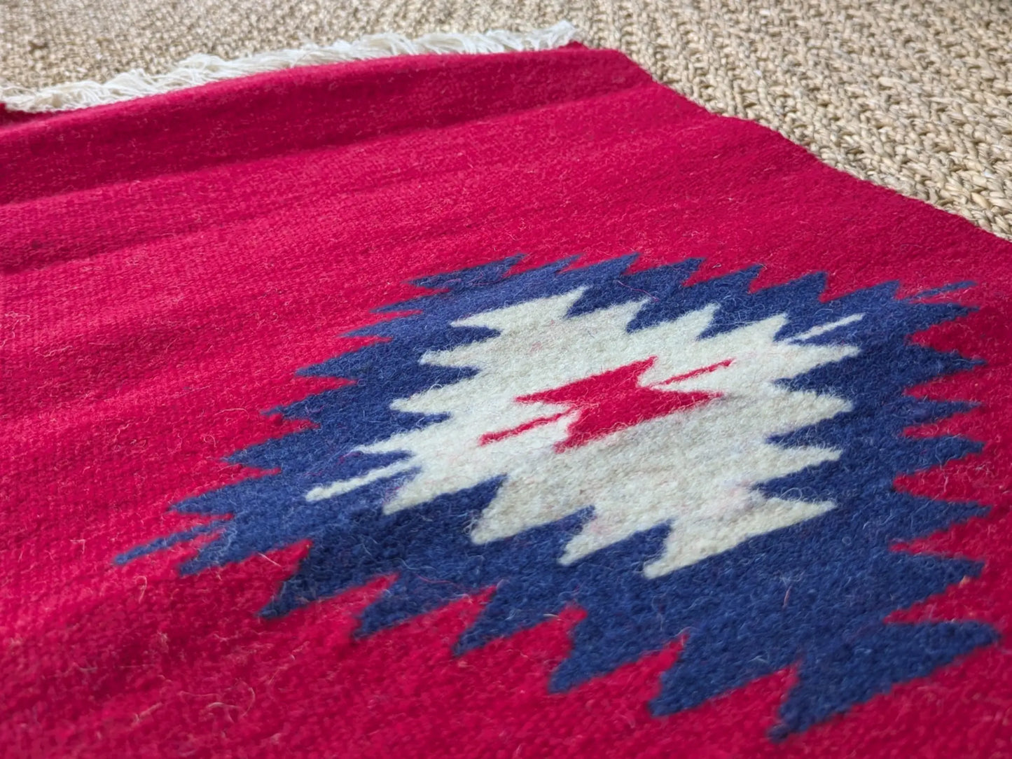 Petit tapis monténégrin rouge en laine avec un losange central. Tissage dense et motif typique des textiles balkaniques.