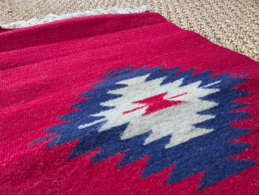 Petit tapis monténégrin rouge en laine avec un losange central. Tissage dense et motif typique des textiles balkaniques.
